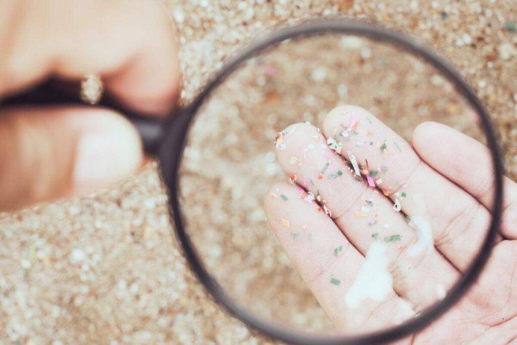 Colorful microplastic fragments on a human palm under a magnifying glass, highlighting the invisible pollution from synthetic textiles